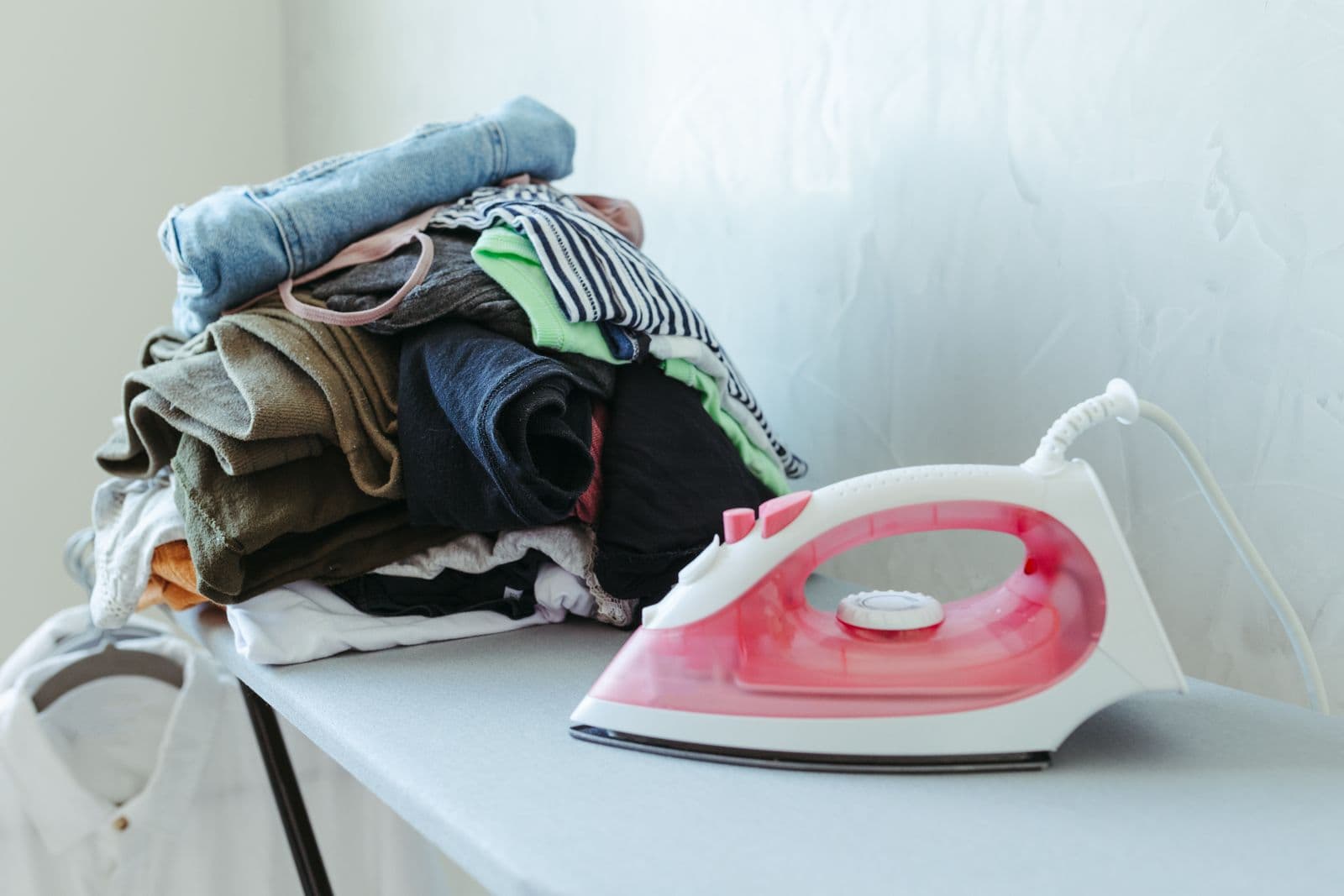 Fer à repasser rose posé près d'une pile de linge sur la planche