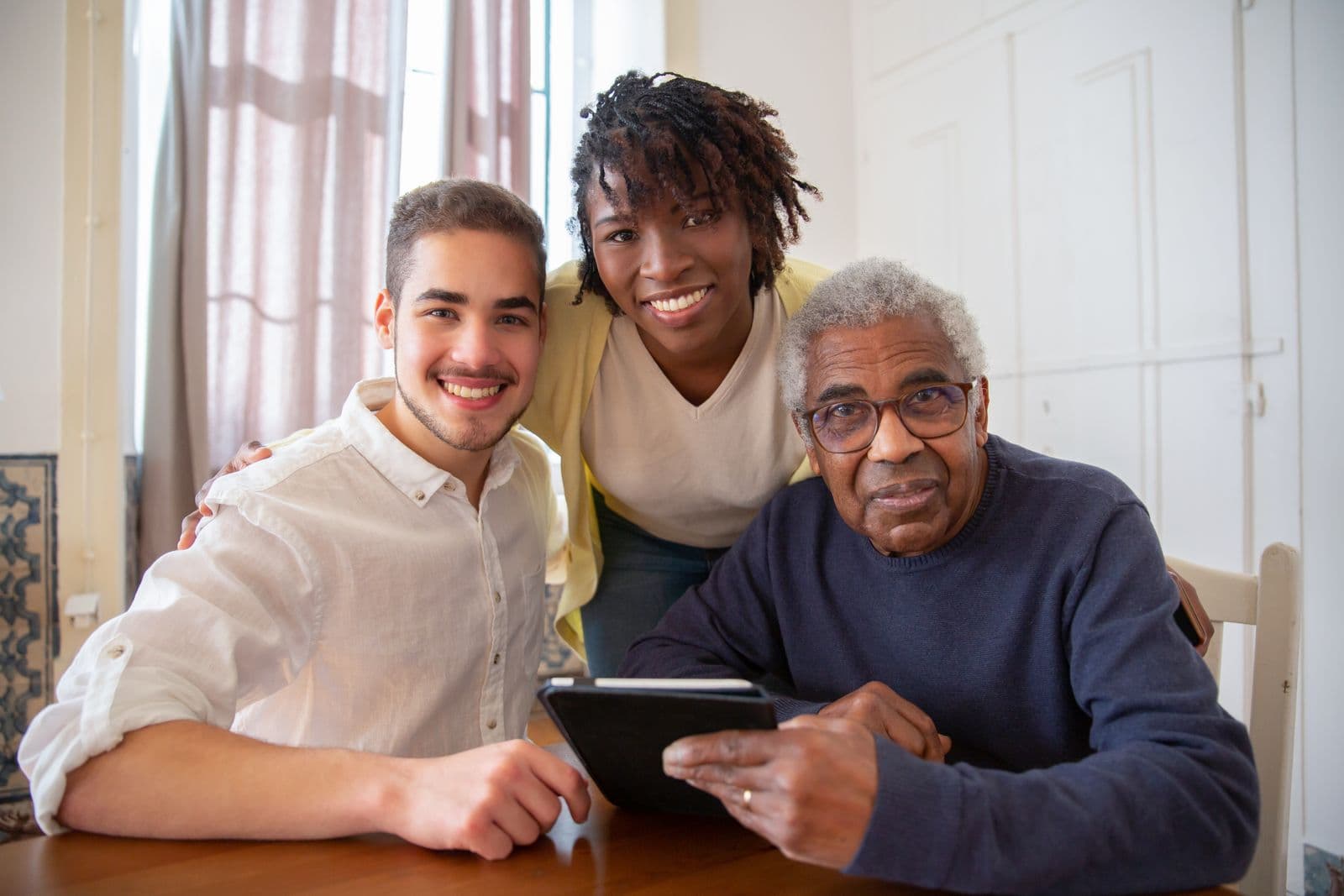 Un monsieur âgé et ses proches réunis autour d'une tablette, tous sourient